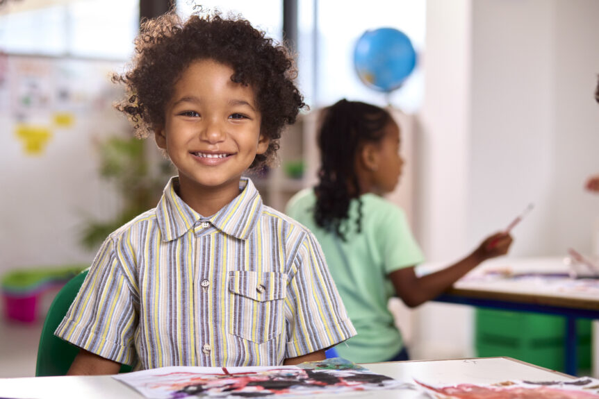 Elementary Student in classroom smiles at teacher.